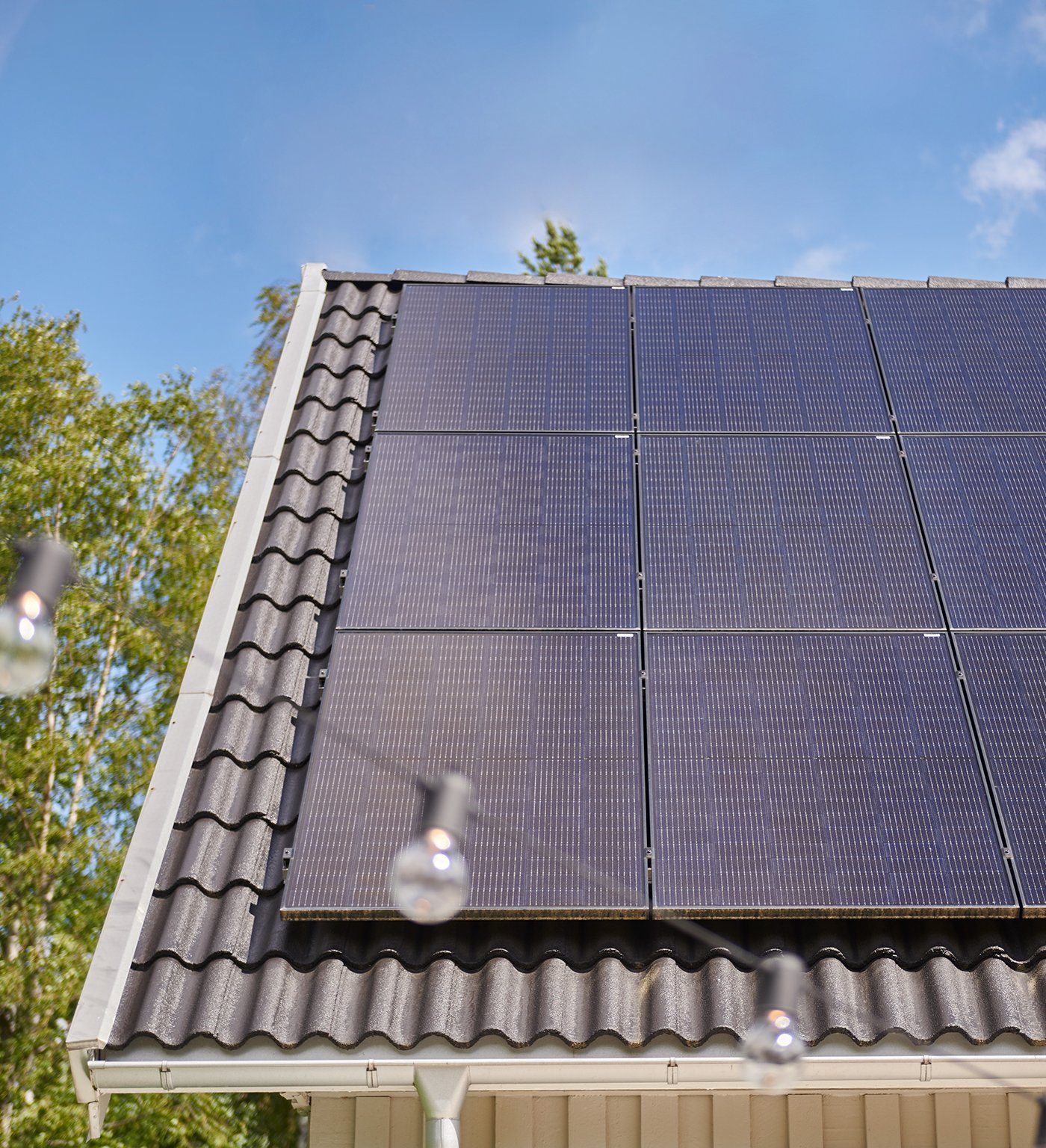 Solar panels mounted on a house roof with brick profiles, with blue sky and trees in the background.