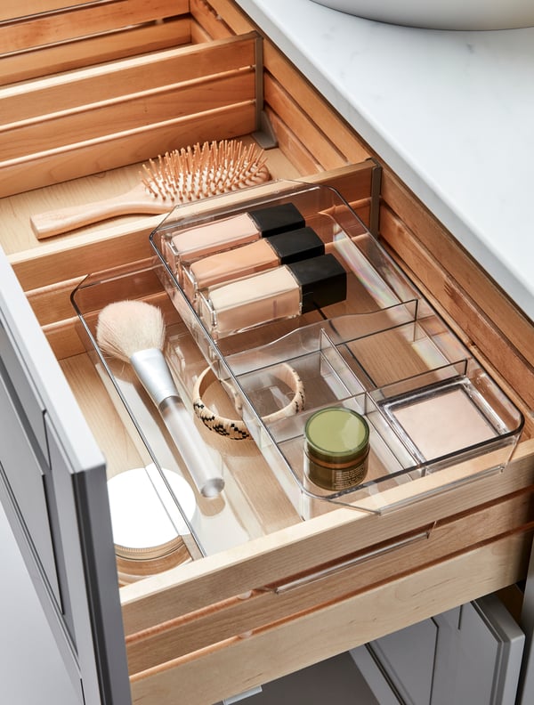 A combination of clear GODMORGON storage boxes filled with bathroom essentials placed in a wooden drawer.
