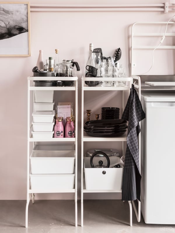 Zwei weisse Servierwagen stehen vor einer Wand in Rosa in einer Küche. In ihnen befinden sich Vorräte und Geschirr.