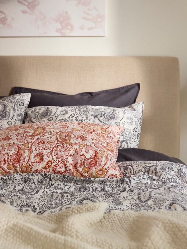 Close-up of bed with RODGERSIA bedding in grey and red paisley pattern.