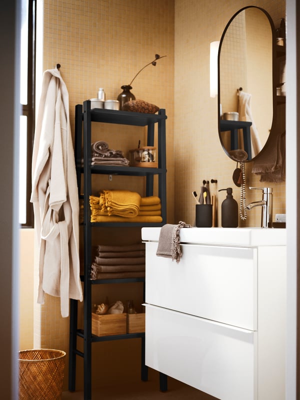 A bathroom with a mirror above a high-gloss white GODMORGON wash-stand with two drawers, a wooden storage unit and towels.