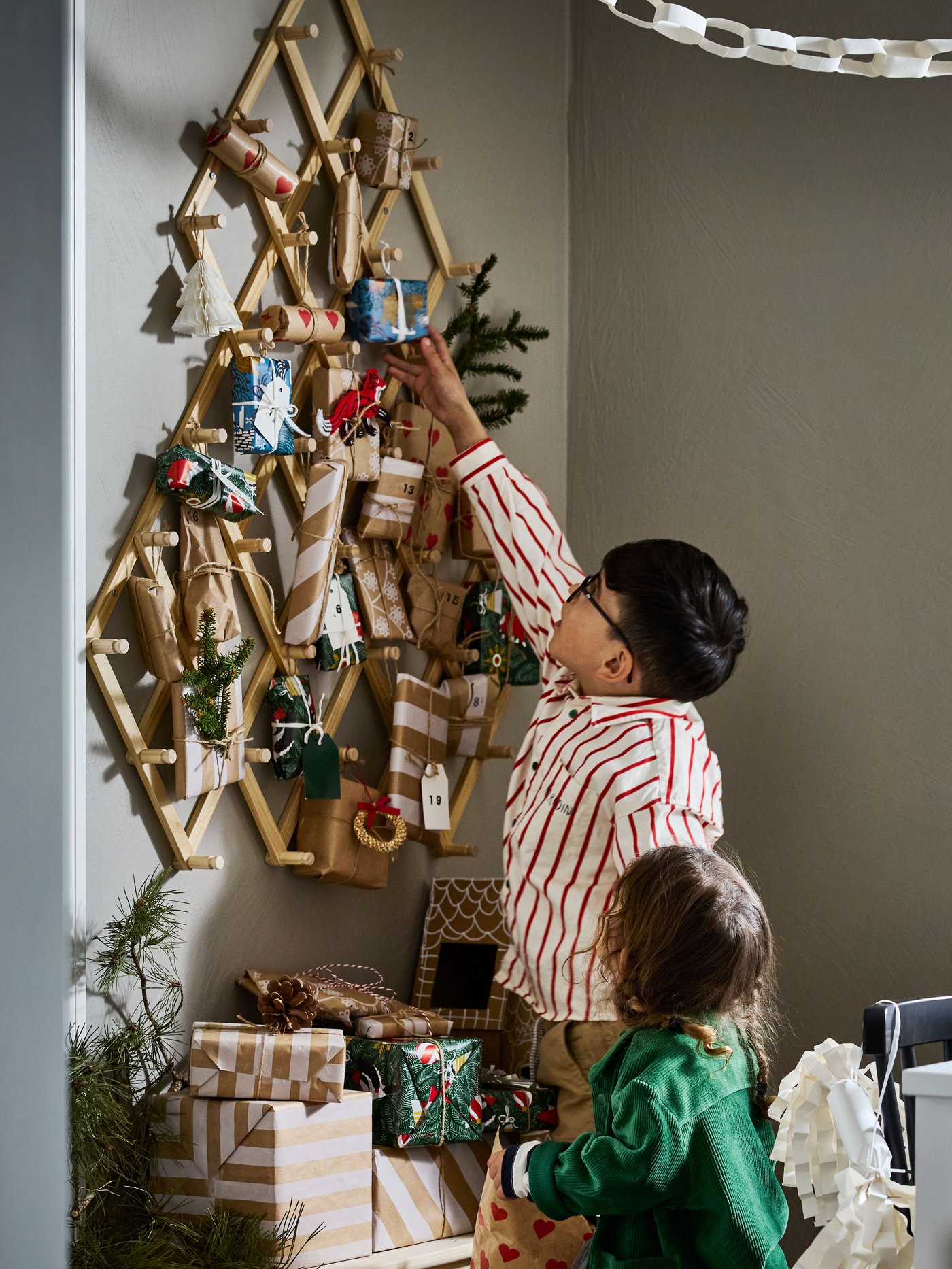 Young brother and sister reaching for an advent calandar present hung from a VINTERFINT wall decoration in pine.