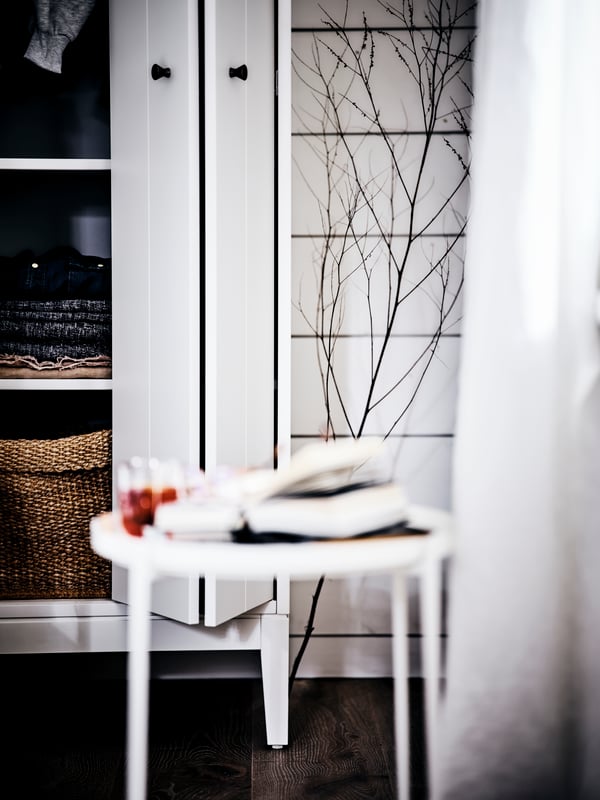 Une table ronde blanche devant une armoire blanche ouverte avec des portes pliantes laissant voir des paniers et des vêtements pliés.