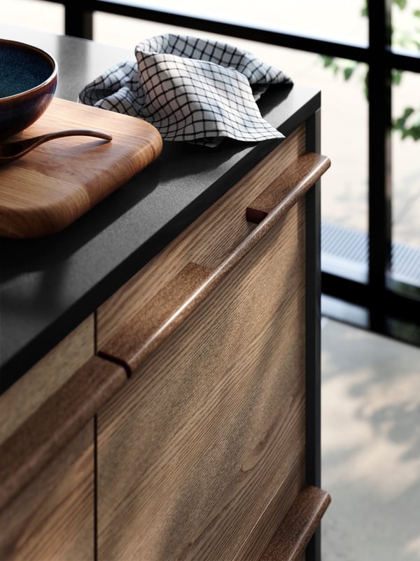 STENSTA dark brown ash veneer drawer fronts, a sleek black countertop, with a wooden cutting board and ceramic bowl on top.