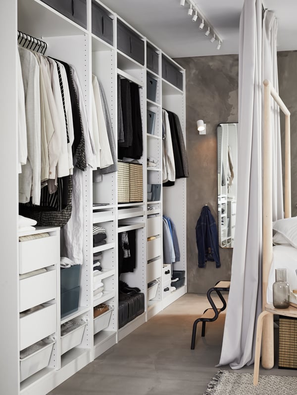 Eine weiße BÄVE LED Deckenschiene mit 5 Spots, daneben ein offenes PAX Kleiderschrank System.
