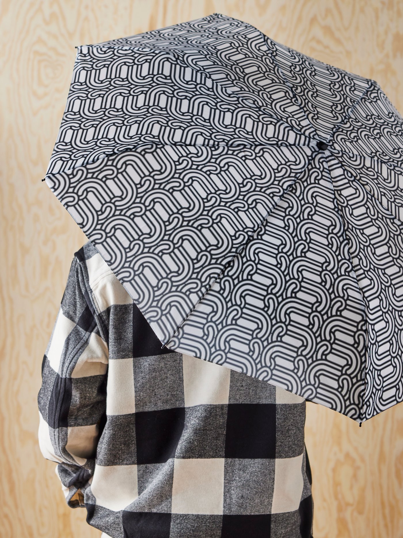 A person wearing a black and white checkered shirt is holding a SÖTRÖNN umbrella with graphic patterns.