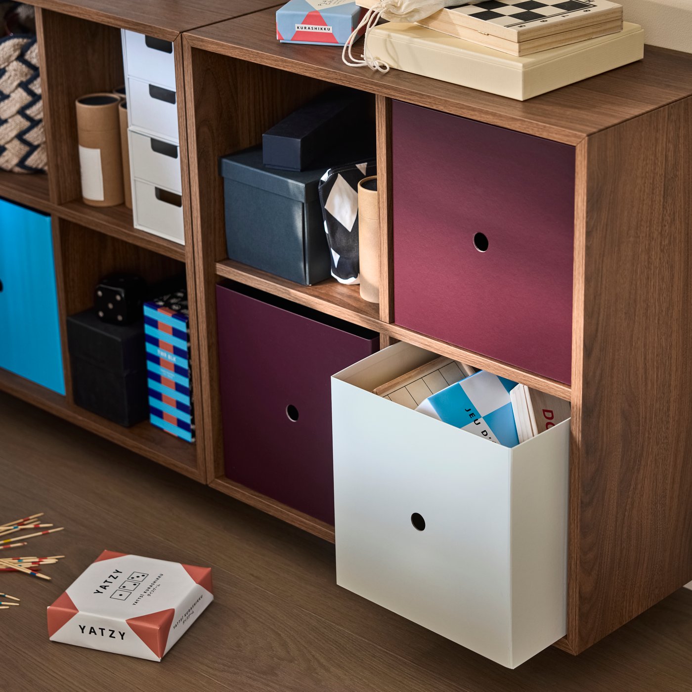 Pulled out from a shelving unit, a SVÅNG box holds papers alongside other storage boxes, books and small items.
