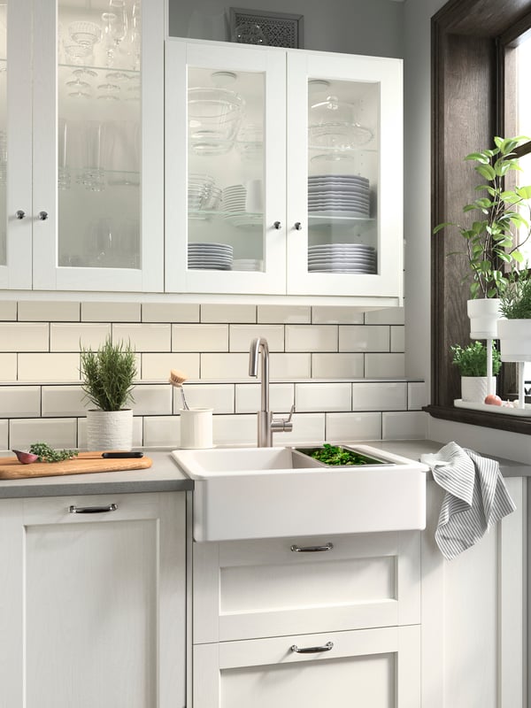 A kitchen with ENKÖPING white fronts, a white HAVSEN sink bowl, wall storage and white plant pots with green herbs growing.