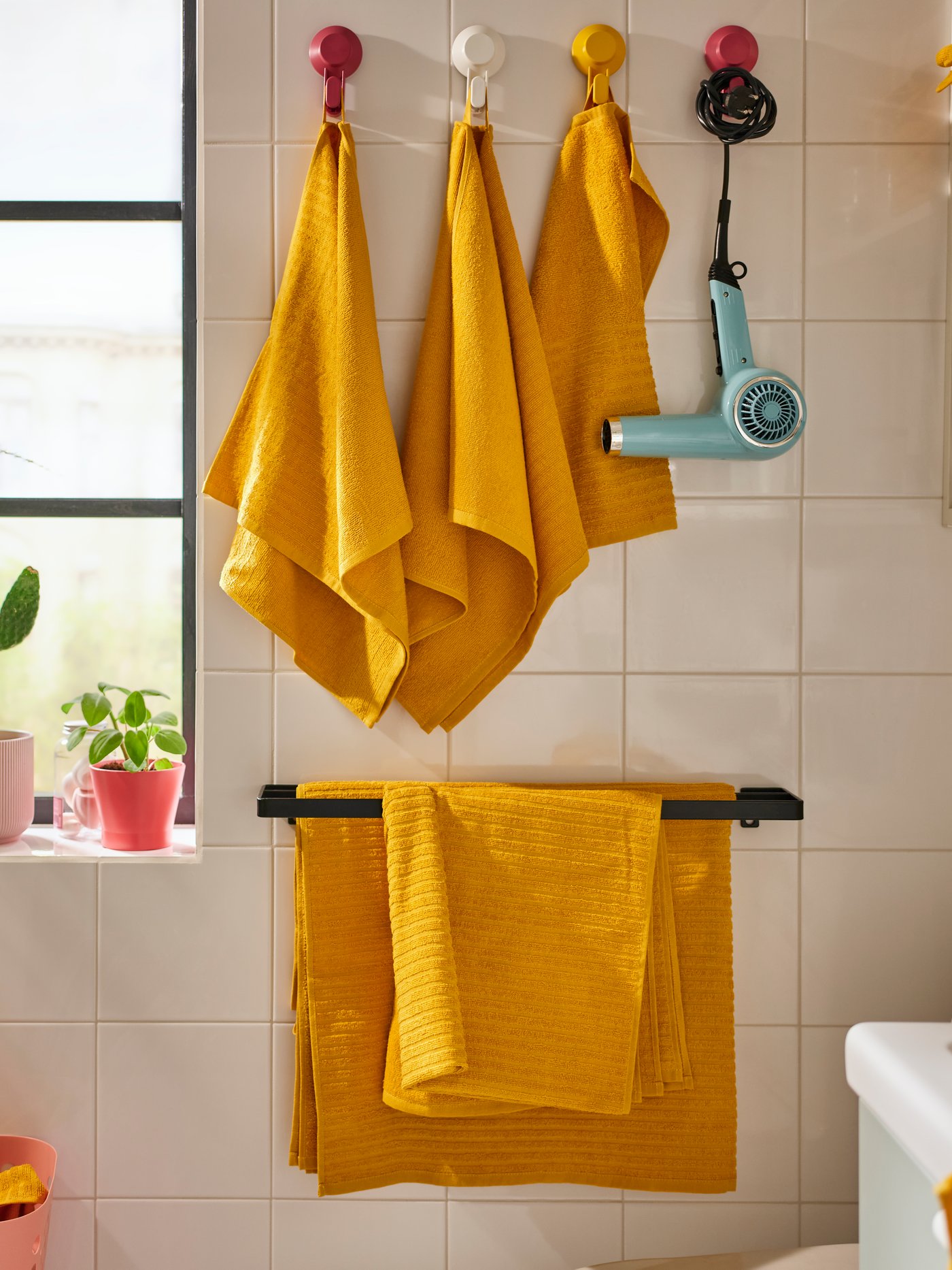un set de toallas VÅGSJÖN amarillas colgadas en unos ganchos de baño.