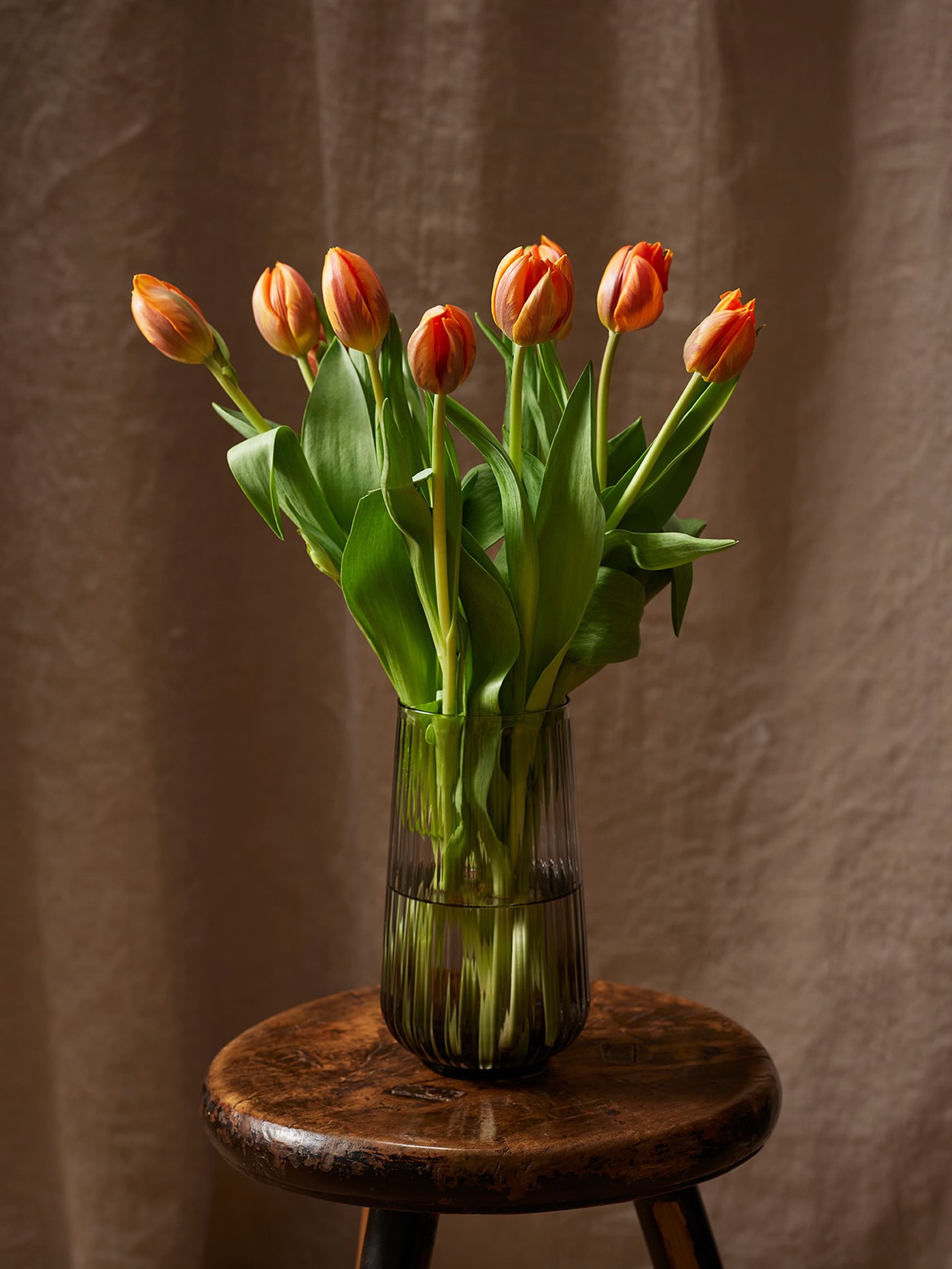 Un florero verde alto de cristal contiene varias flores de tulipán.