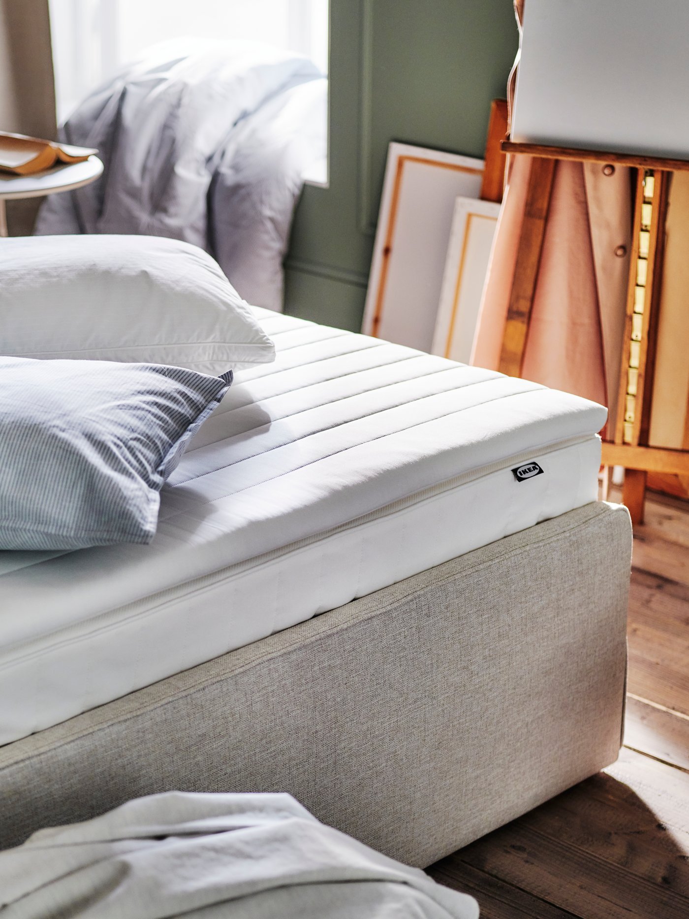 A VESTRÖY hybrid mattress on a beige RAMNEFJÄLL upholstered bed. A NÄSFJÄLLET mattress pad and GRÖNAMARANT pillow are on top.