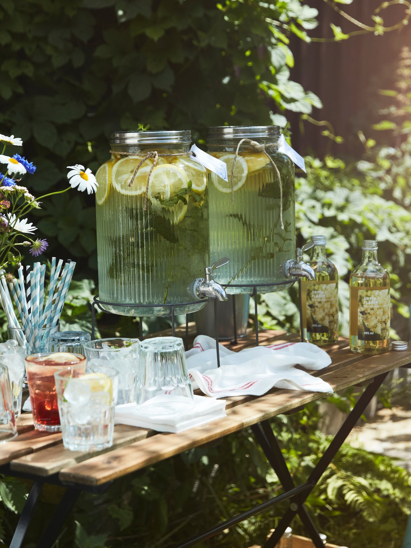 Chargée de verres, de pailles et d’une fontaine à boisson VARDAGEN remplie de limonade, une petite table de jardin est prête à accueillir les invités.