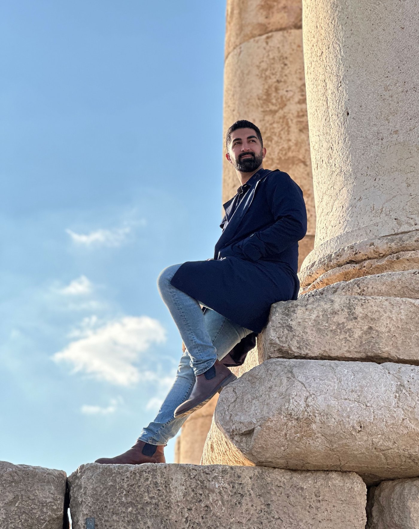 Arash à l’extérieur par une journée ensoleillée, appuyé sur une grande colonne.