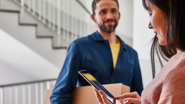 A delivery man hands a parcel to a customer in the stairwell