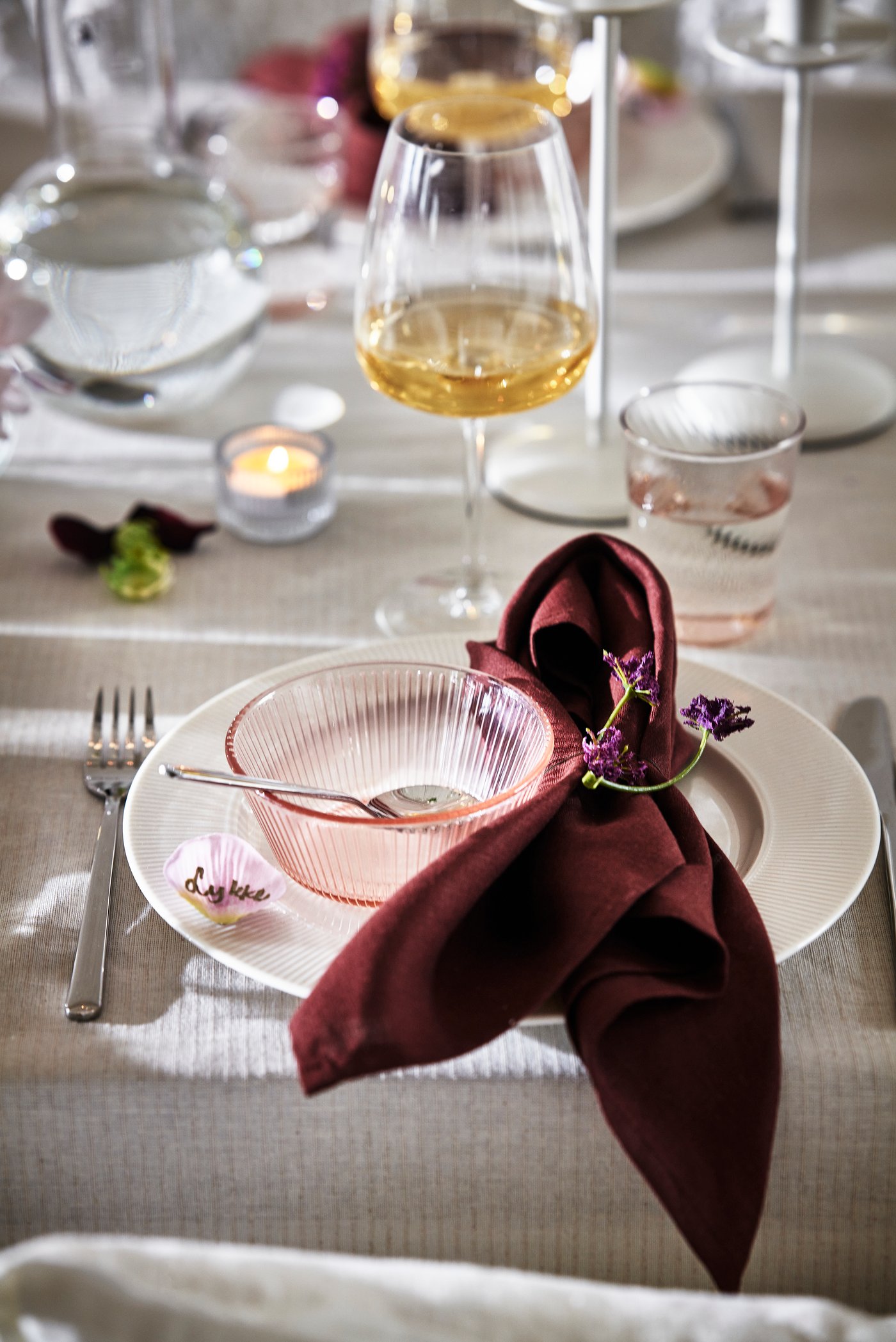 En vinröd handduk bredvid en skål i ljus rosa glas.