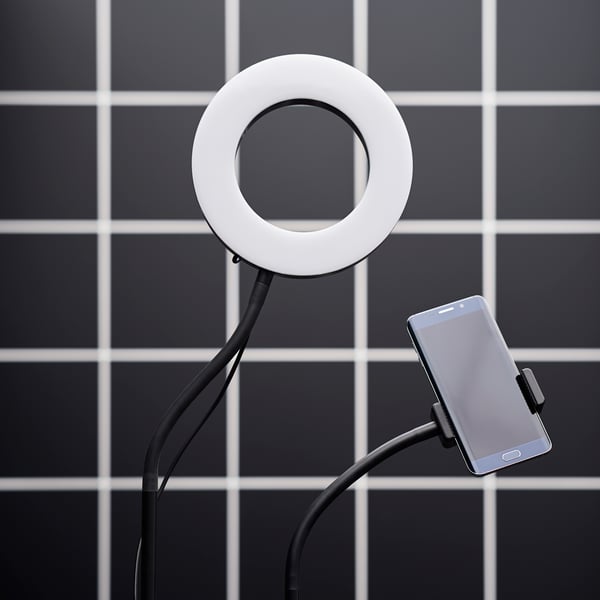 Ring light and mobile phone holder against a black tiled backdrop.