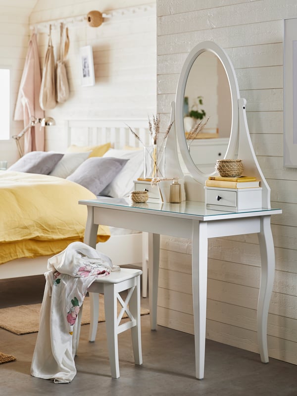 White HEmnes dressing table with rattan boxes on top. Next to it is a bed with a yellow duvet cover and in front of it a white bench with a blanket on top.
