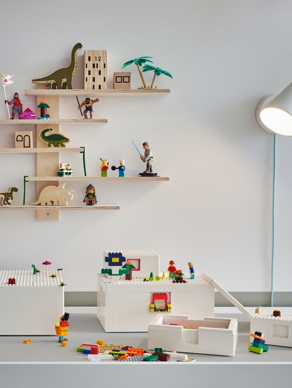 Na stole DUNDRA jsou kostky a krabice BYGGLEK LEGO®. Na stěně za stolem je lampa a nástěnná police LUSTIGT.