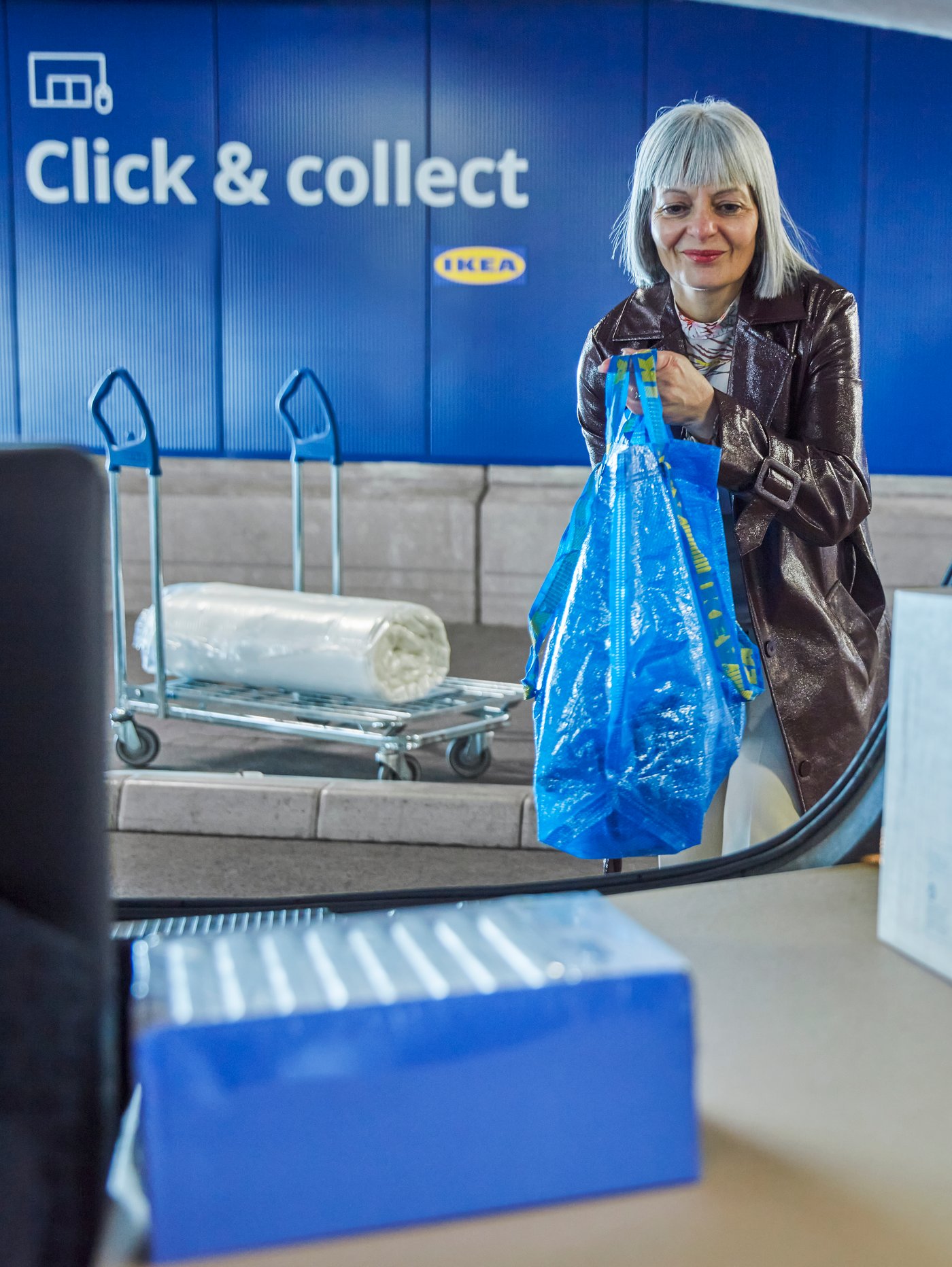 Eine Person von vorn, wie sie ihre Click & Collect Bestellung in den Kofferraum eines Autos einlädt.