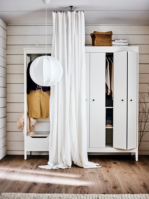 Two white IDANÄS wardrobes with a REGNSKUR/SUNNEBY pendant lamp and a DYTÅG curtain hanging in front of them.