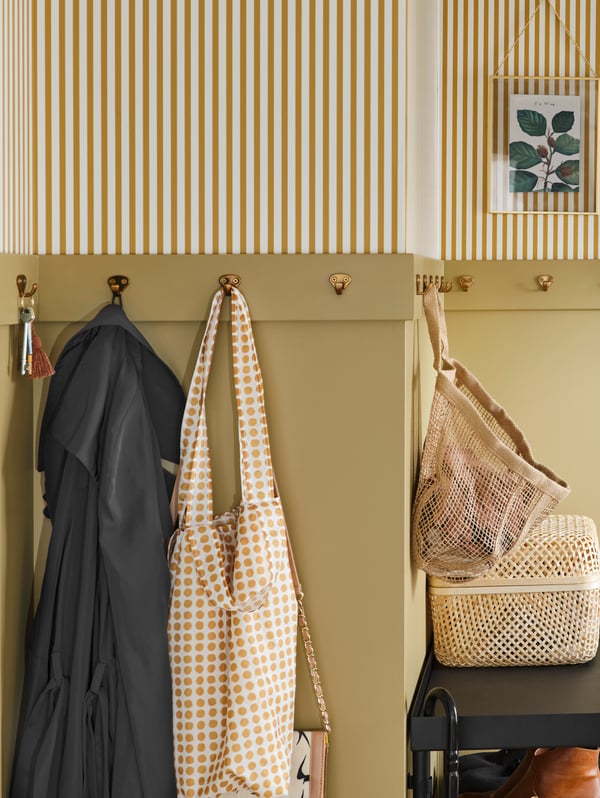 A row of KVAST hooks go around the wall of a hallway. Keys, clothes and a LUSTIGKURRE bag hang from the hooks.