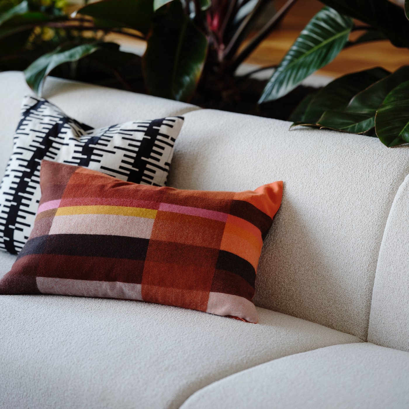 Two cushions resting on a beige sofa, one of them with a brown-red and bright pink STOCKHOLM 2025 cushion cover.