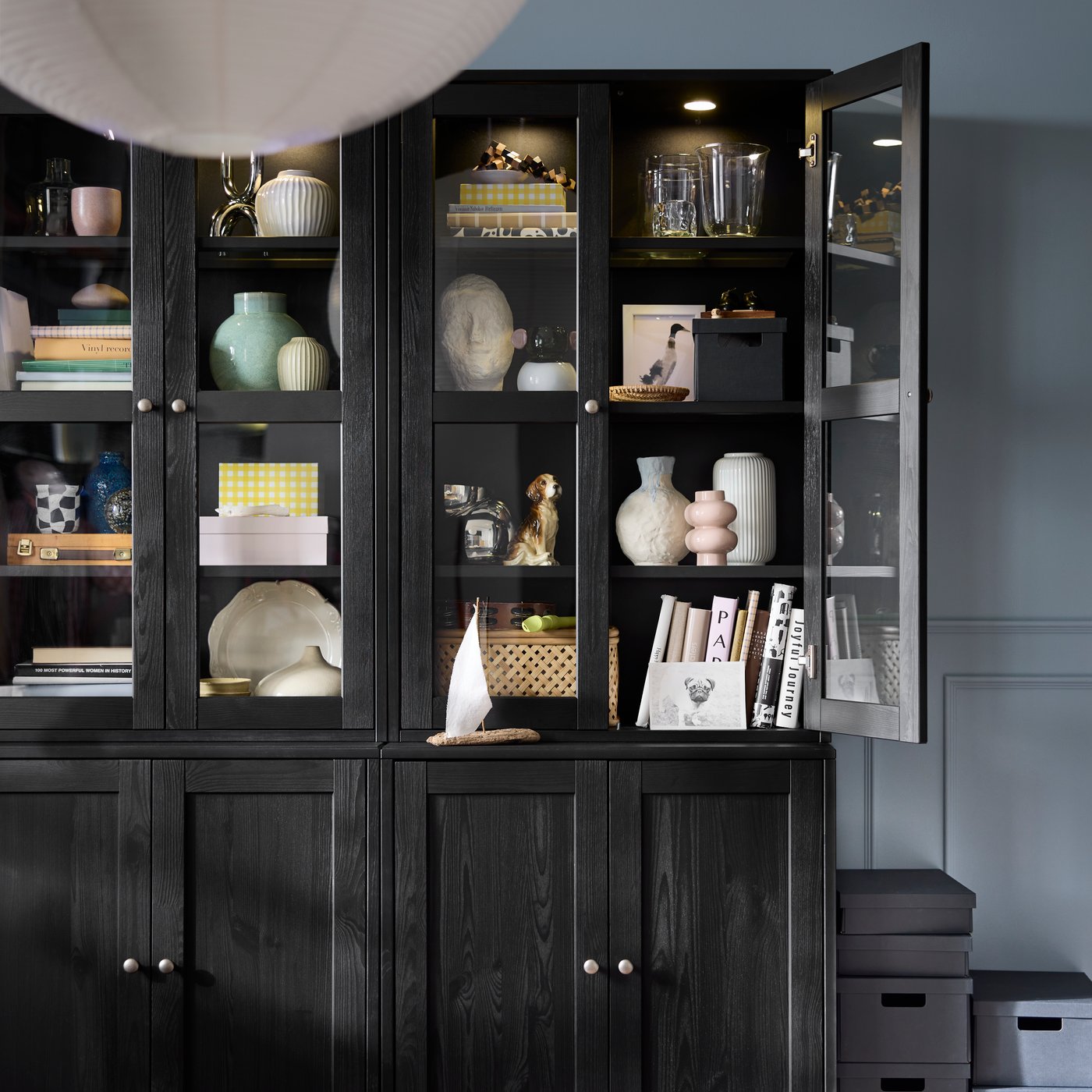 Side-by-side black HAVSTA storage units with glass-door sections densely yet tidily arranged with decoration and accessories.
