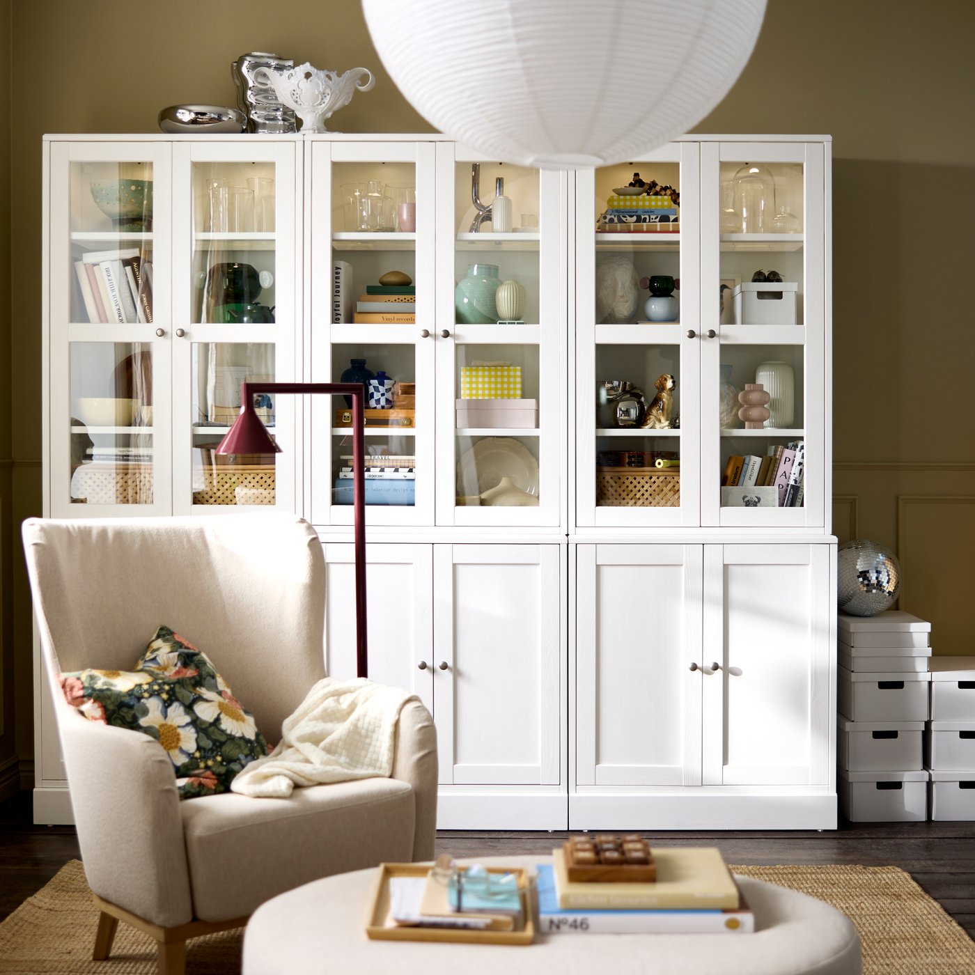 Una sala de estar con una combinación de almacenamiento HAVSTA blanca con puertas de vidrio, que exhibe objetos decorativos y libros.