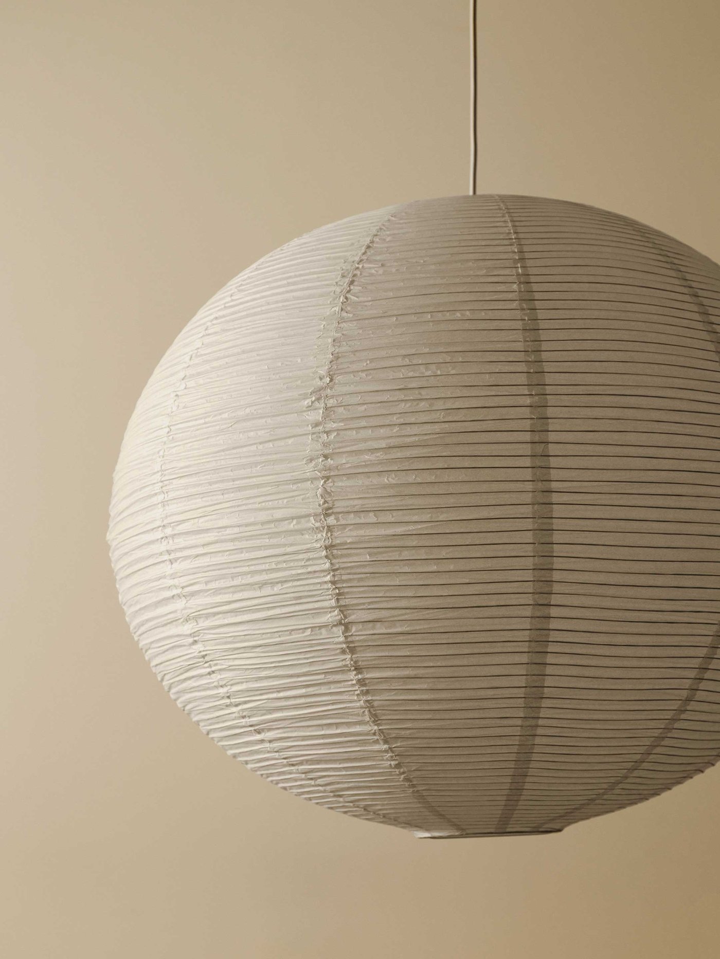 En vit GULLSUDARE-rispapperlampa mot en beige bakgrund.