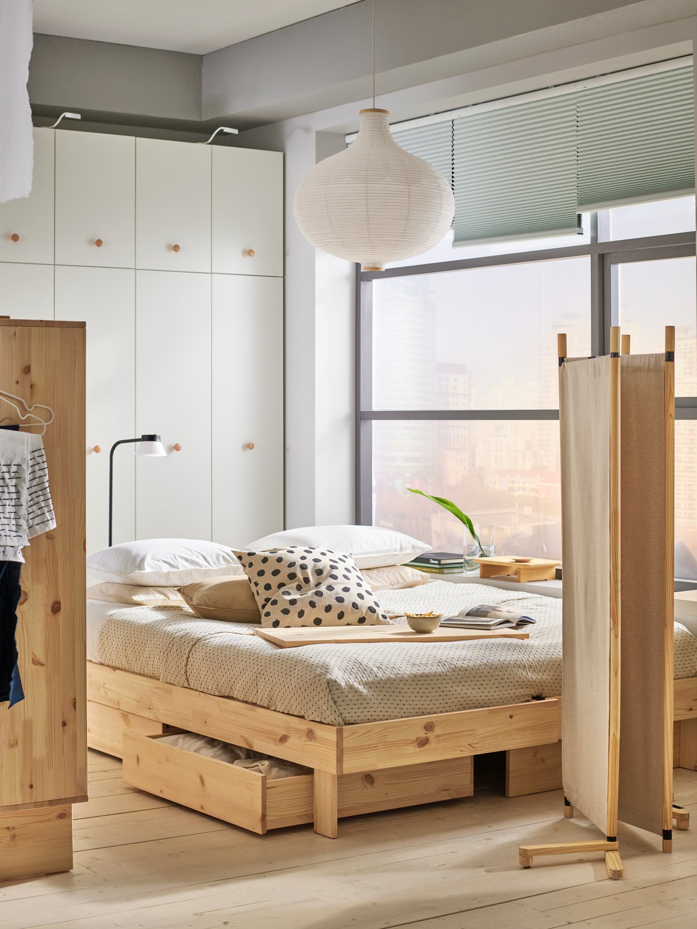 Soveværelse i beige farver med GLAMBERGET seng, garderobe og rumdeler i naturtræ.