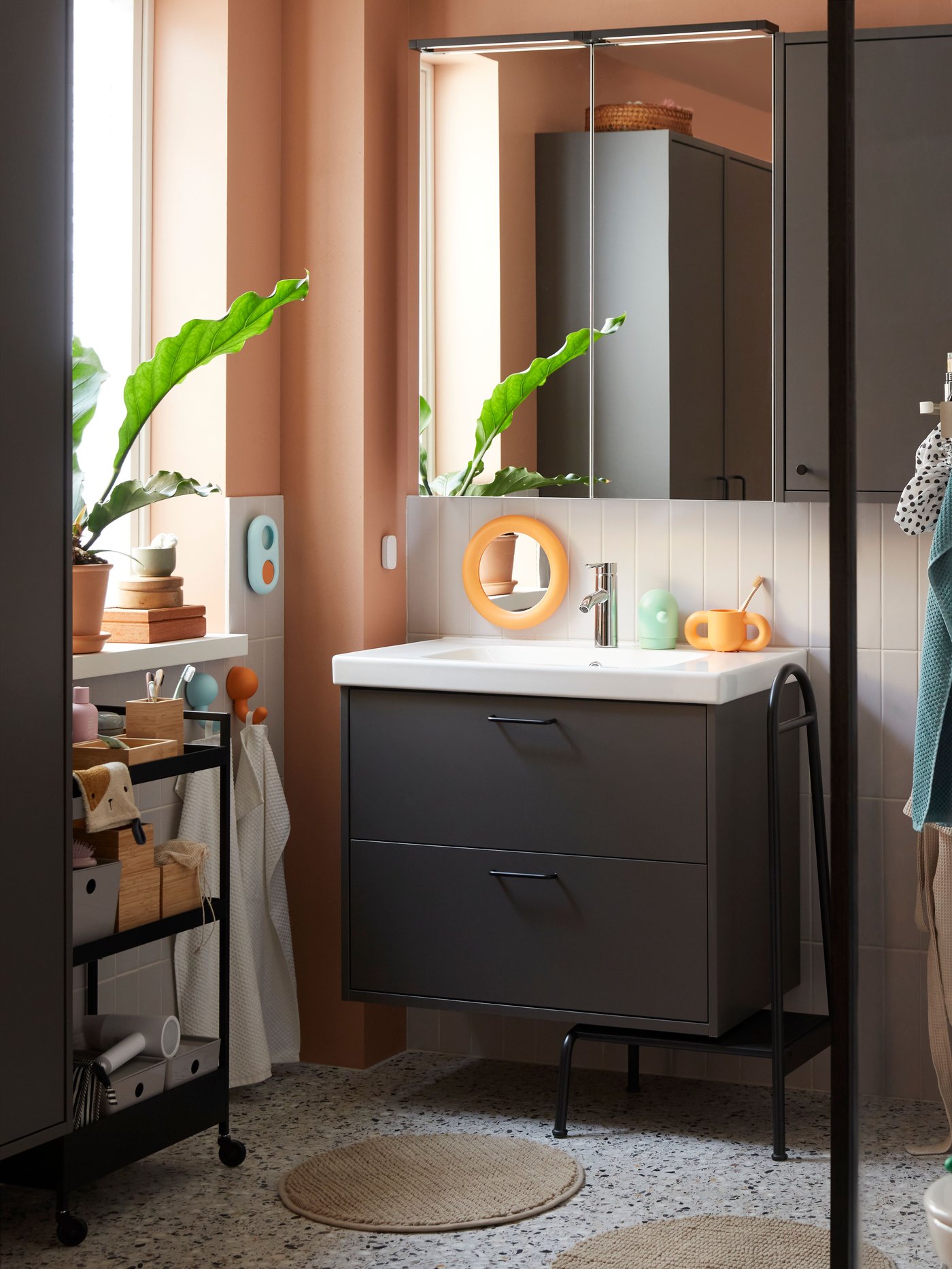 Ein LETTAN Spiegelschrank und ein orange-türkisfarbener HUMLESJÖN-Haken mit Saugnapf im Badezimmer.