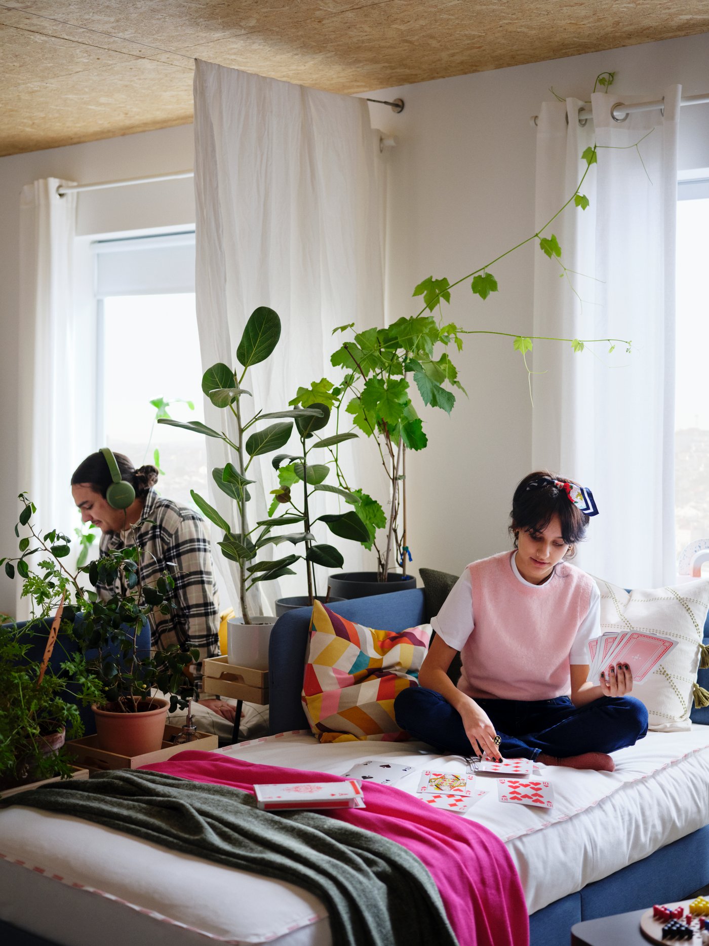 A teenager sitting on a single bed with plants in the background