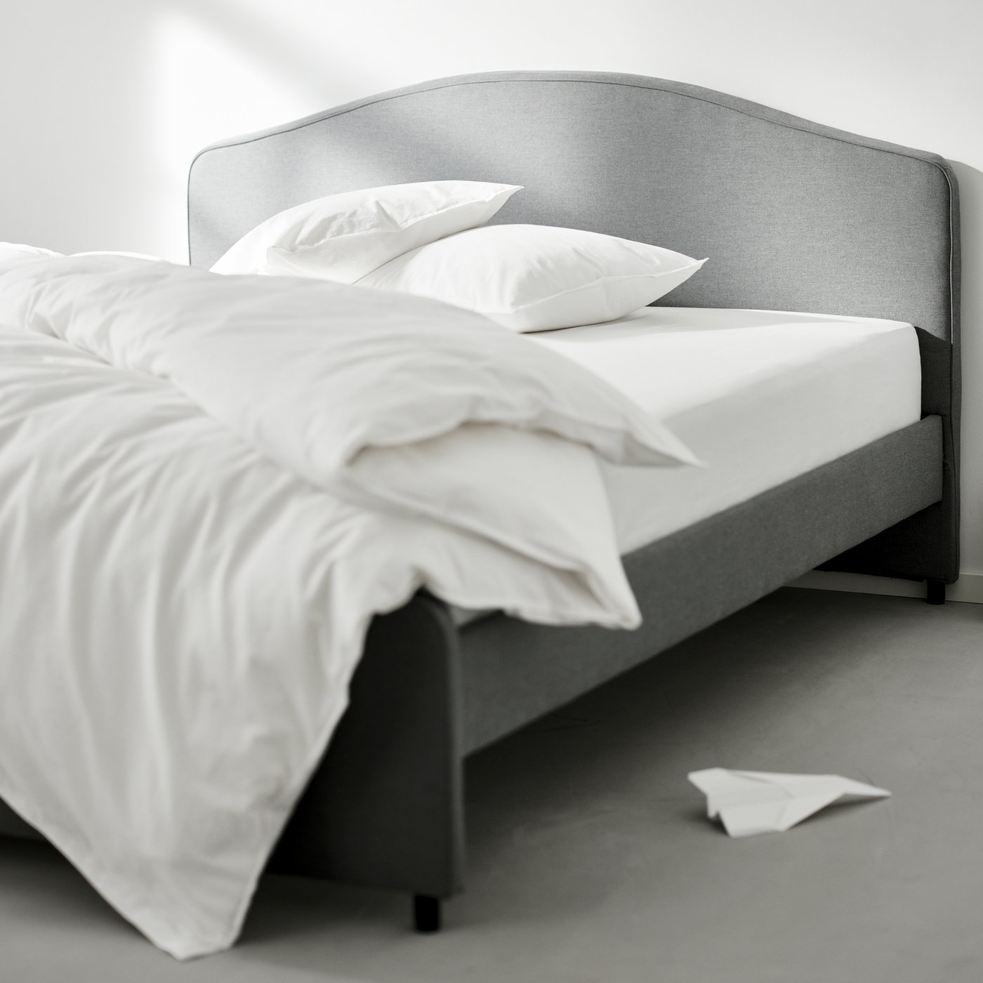 A grey HAUGA upholstered bed with two pillows at the top and a duvet folded over at the bottom, covered in white bed linen.