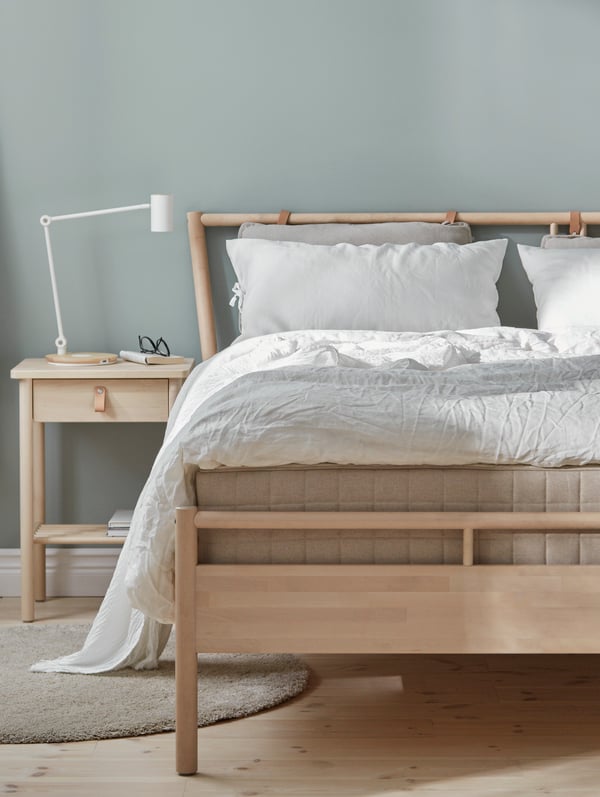 A bedroom with grey walls containing a bed with a BJÖRKSNÄS bed frame in birch, a bedside table in birch and white bed linen.