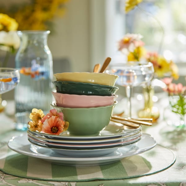 Pile de bols jaunes, verts et roses, sur de petites assiettes blanches et un set de table à rayures blanc et vert.