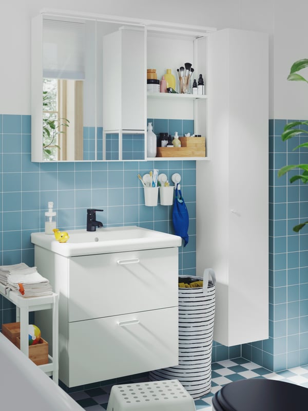 A blue-tiled bathroom with a bathtub has a white ENHET vanity, a mirror cabinet, a high cabinet and a VESKEN cart.