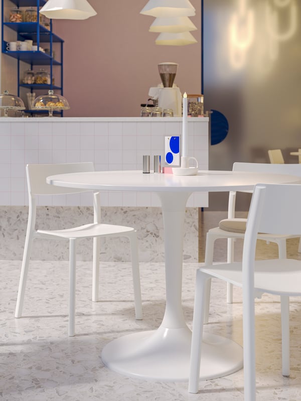 Un tavolo DOCKSTA bianco e sedie JANINGE bianche accanto a un angolo bar con articoli per servire in tavola su scaffali a giorno PLATSA blu.