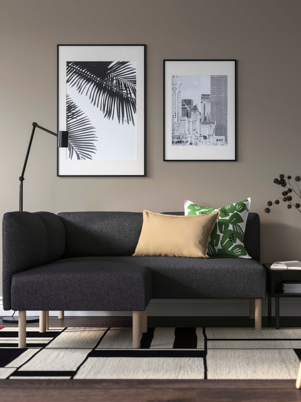 Moderner IKEA-Wohnbereich mit dunkelgrauem Ecksofa, gemustertem Teppich, dekorativen Kissen und stilvollen Bilderrahmen – skandinavisches Design für ein gemütliches Zuhause.