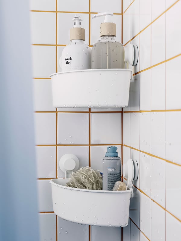 Two white TISKEN corner shelf units with suction cups with bottles inside are attached to a white-tiled shower wall.