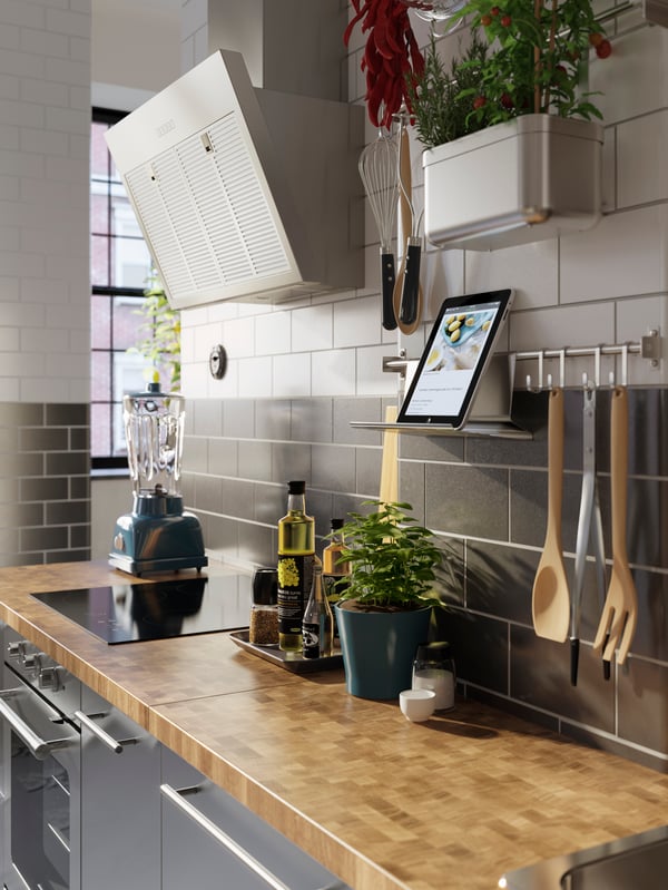 A kitchen counter with a rail on the wall above holding a tablet on a tablet stand. Cooking utensils hang from the rail.
