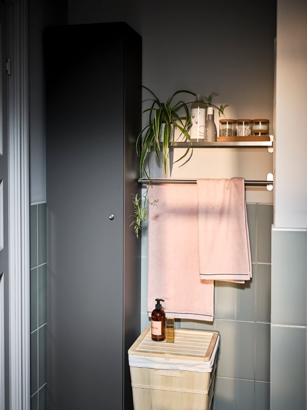 A section of a tiled bathroom with a dark-grey GODMORGON high cabinet and light-pink hand towels on a BROGRUND towel rail.