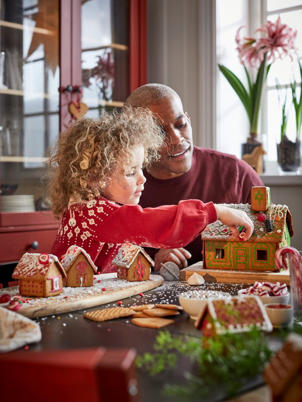 Young girl and father decorating traditional Swedish VINTERSAGA gingerbread house at Christmas.