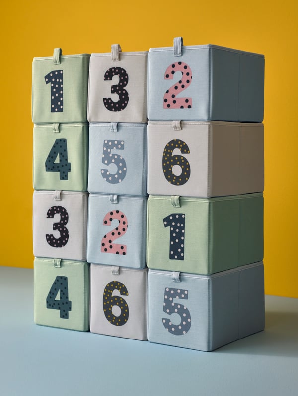 Twelve BARNDRÖM boxes in different colours with numbers on are stacked on top of each other against a yellow background.