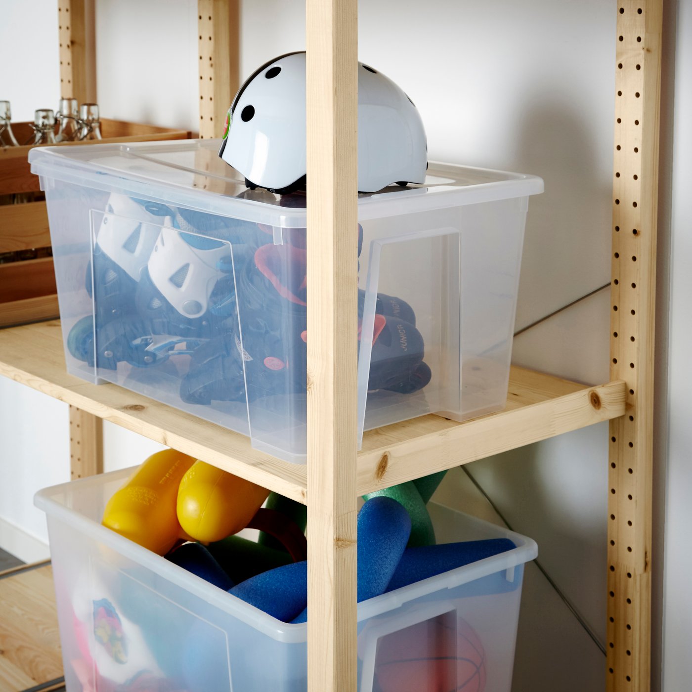 Wooden shelving unit with clear plastic storage bins containing assorted household items in an organized storage area.