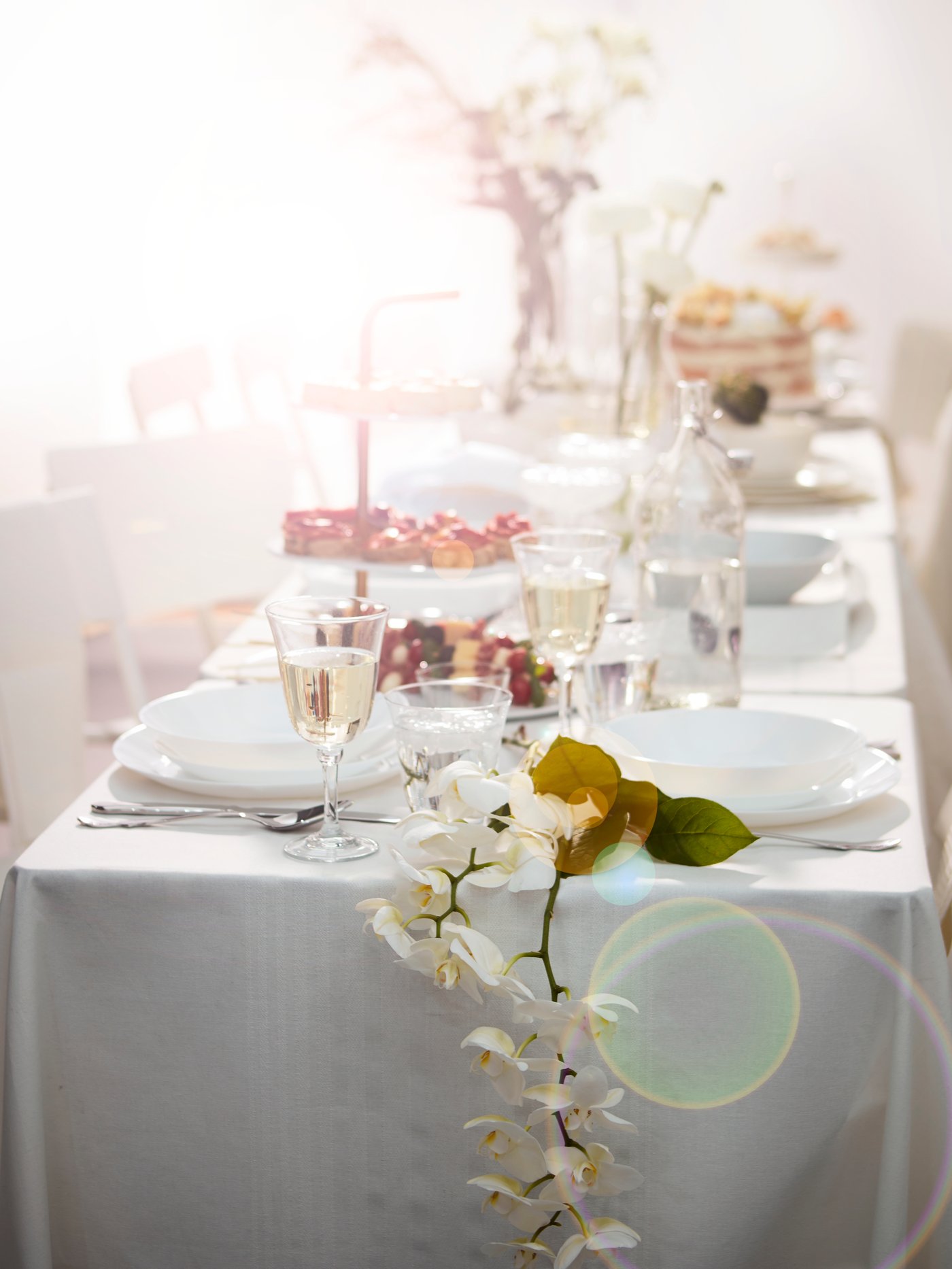 Et bord er dækket med en hvid dug, og der er blomster og glas på bordet.