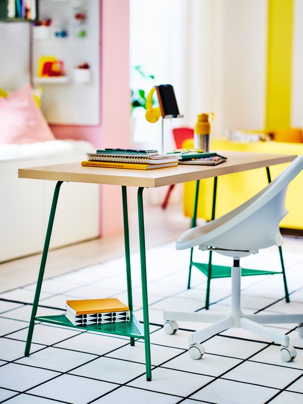 A vibrantly coloured space with a swivel chair and a slim-legged table in the middle, placed on a geometric-pattern rug.