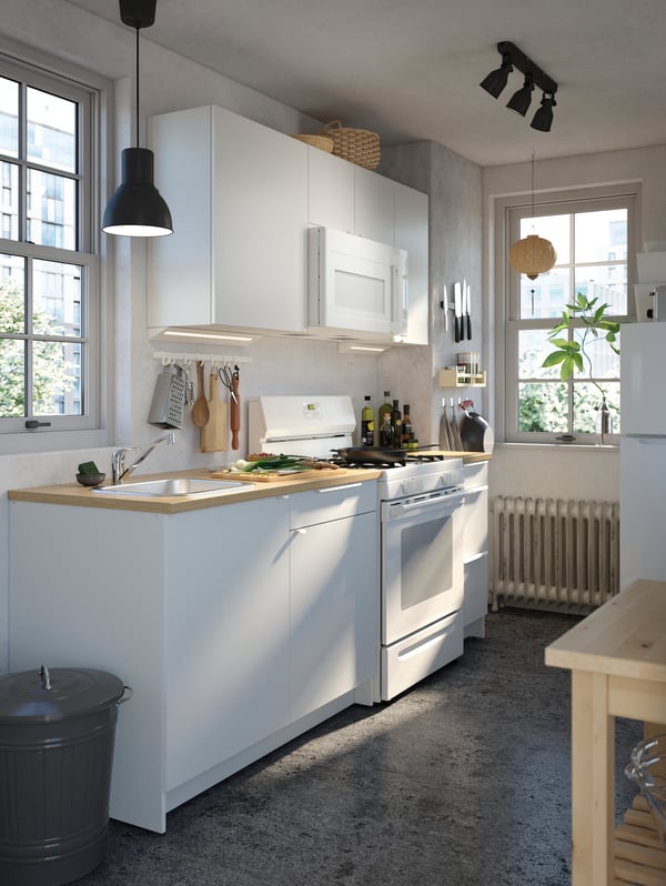 A KNOXHULT kitchen in white with various items on the worktop, a HEKTAR pendant lamp in dark grey and a kitchen trolley.