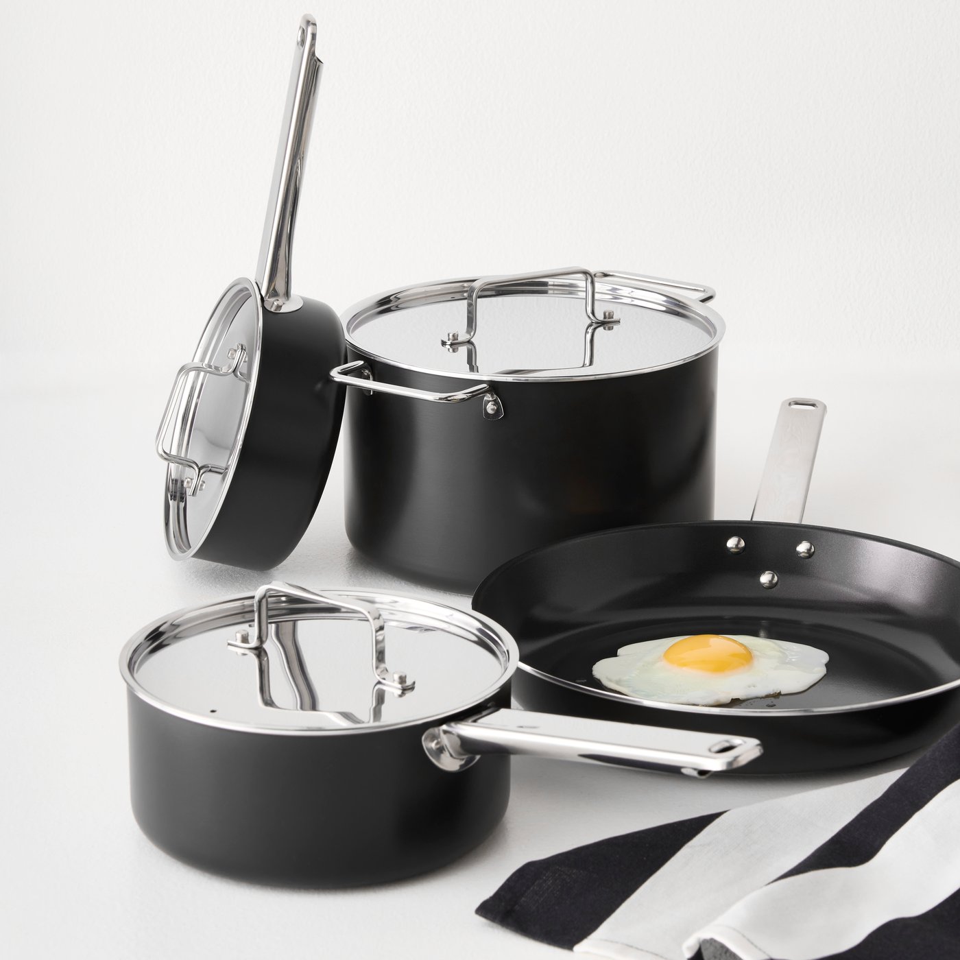 A white countertop with a black-grey GULDÖRING 7-piece cookware set, featuring non-stick stainless steel pots and frying pan