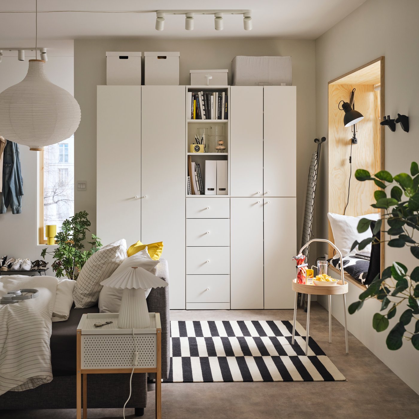 A living space with a LASTARE wardrobe combination alongside a sofa, indoor plants and a black-and-white striped rug.