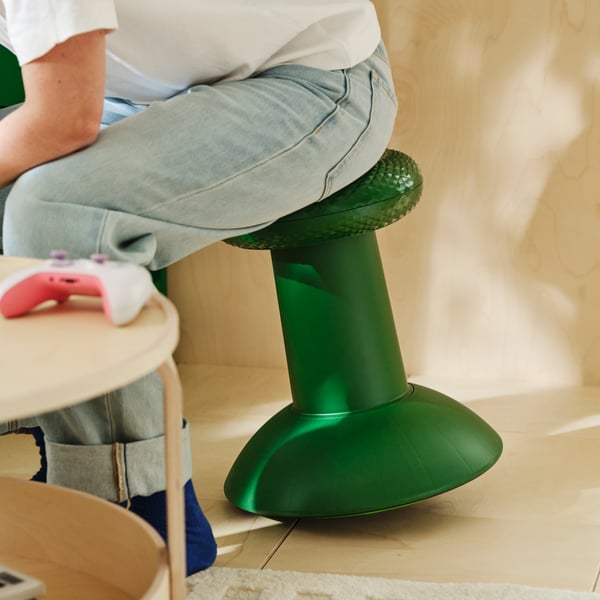 A person sits on a green YXSTABY gaming thumbstick stool, leaning forward.